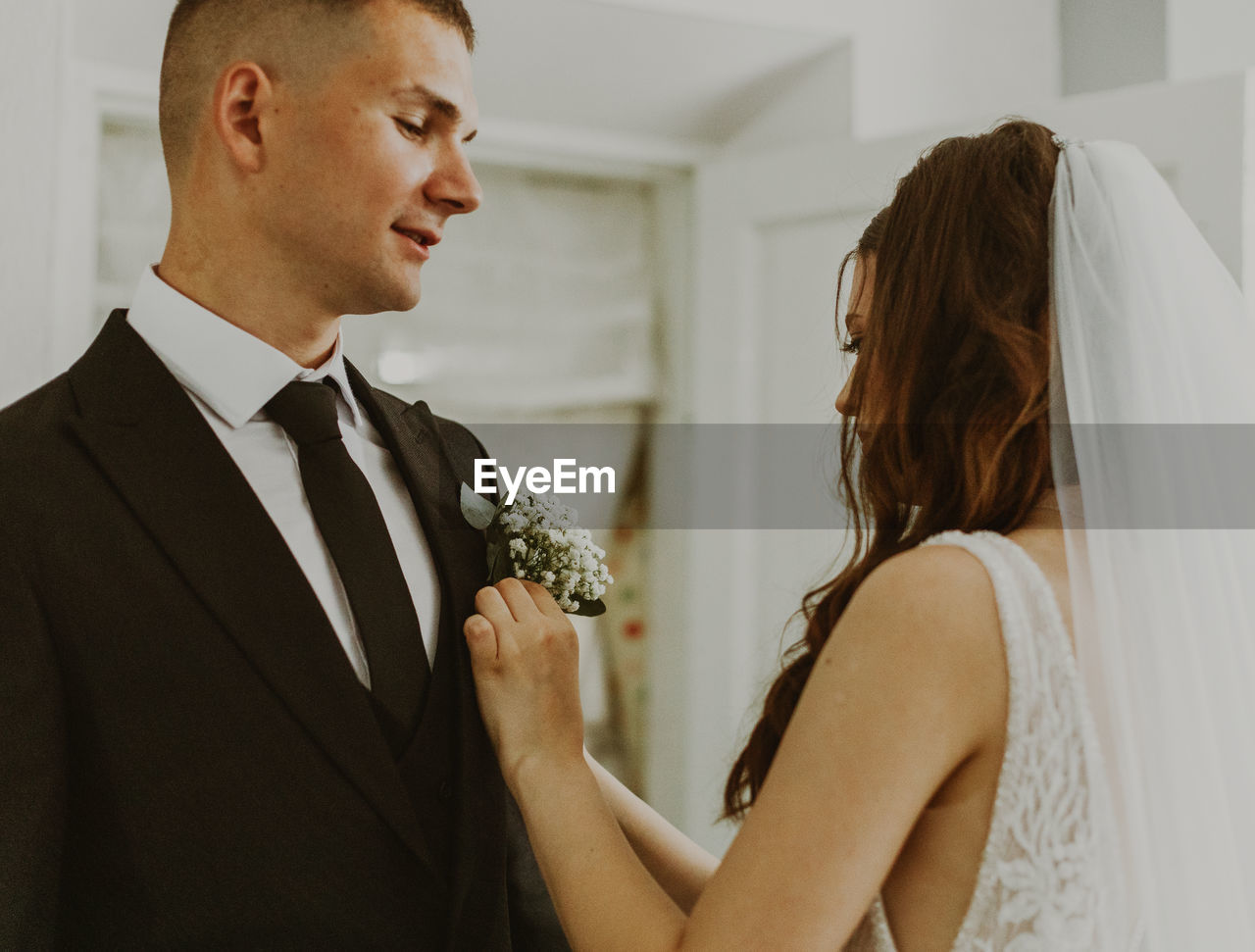 A beautiful bride inserts a bouquet of boutonnieres into the groom's jacket pocket.