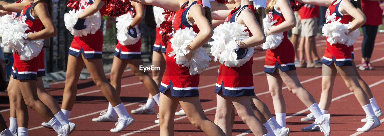 A group of high school cheerleaders during a high school football game using red and white pom poms.