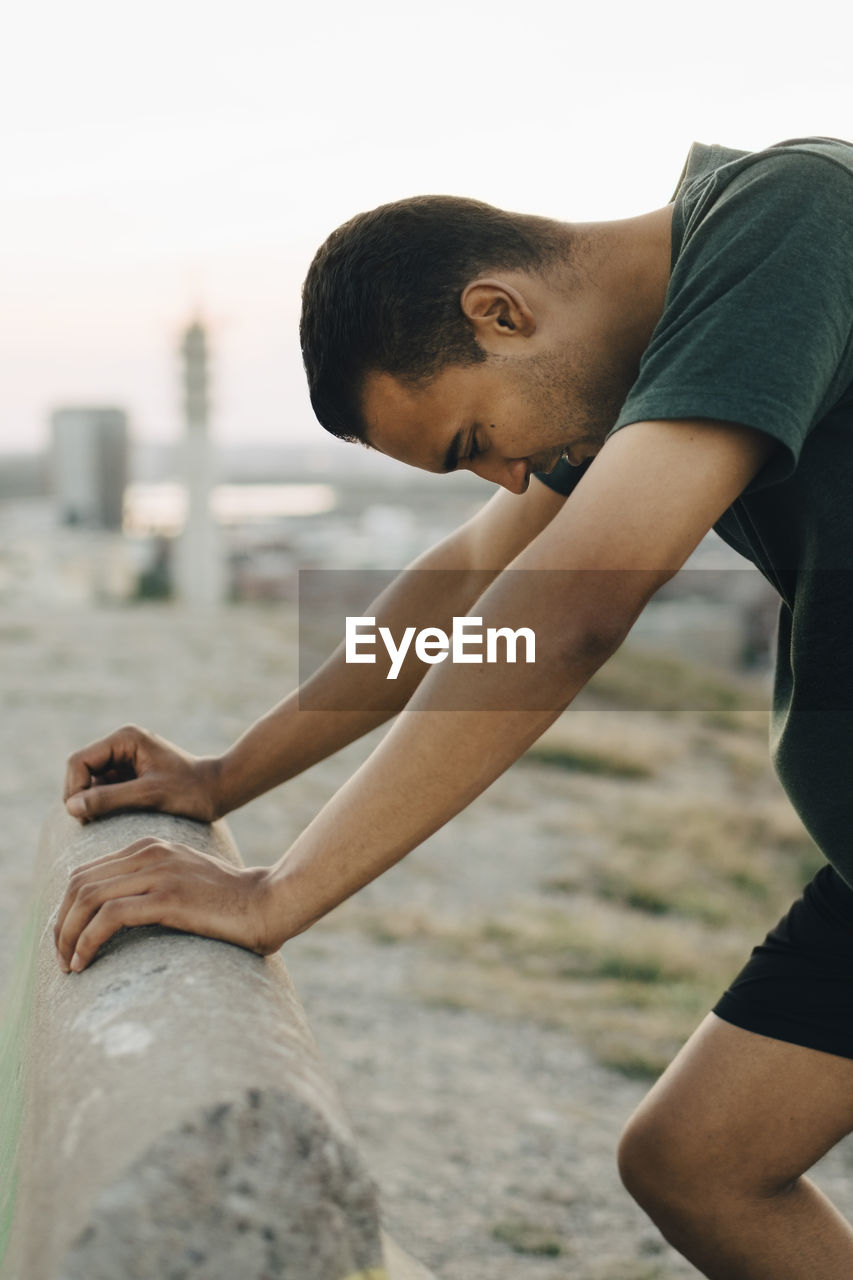 Young male athlete leaning on retaining wall during sunset