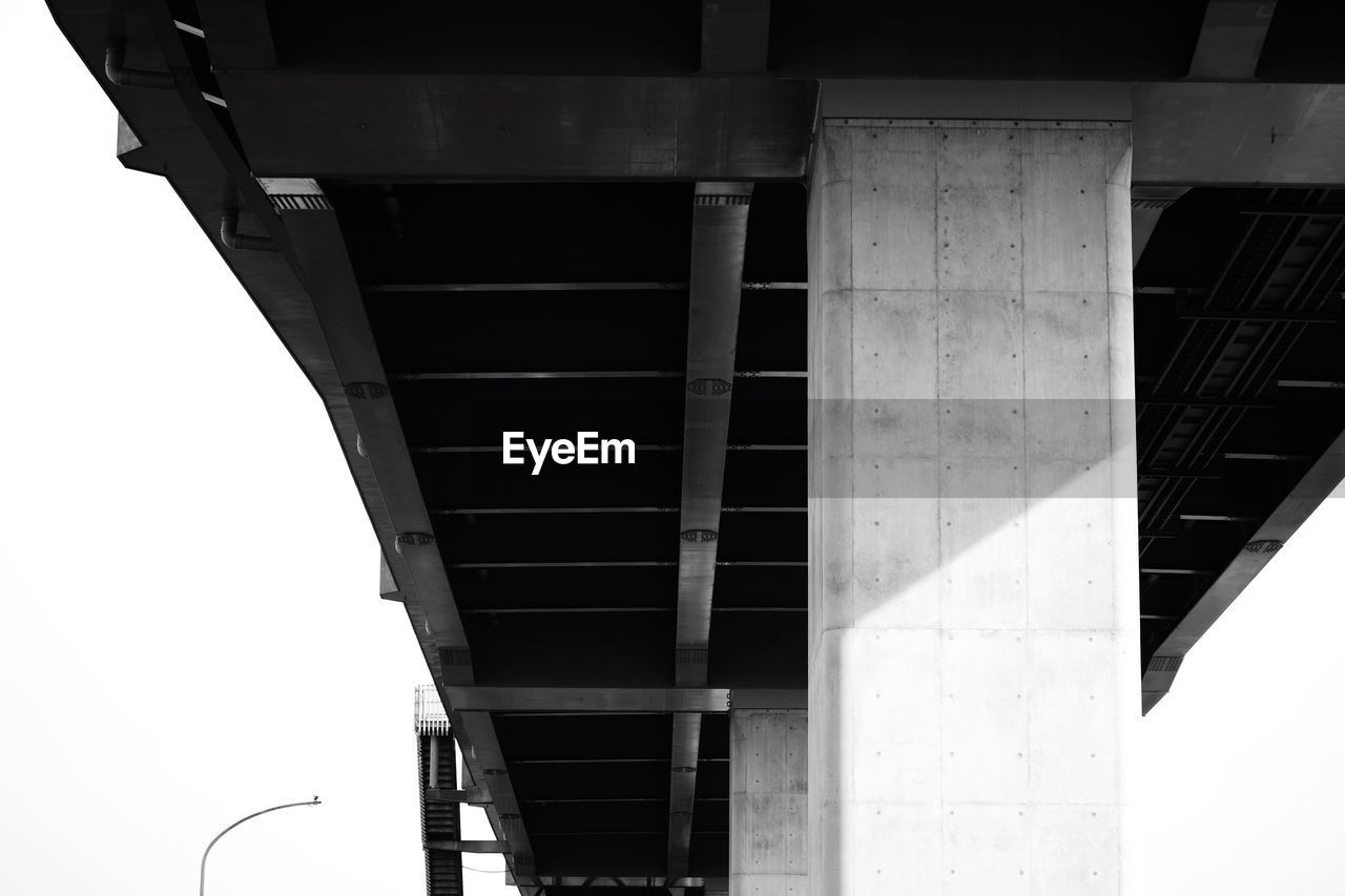 LOW ANGLE VIEW OF BRIDGE OVER ROAD AGAINST BUILDINGS