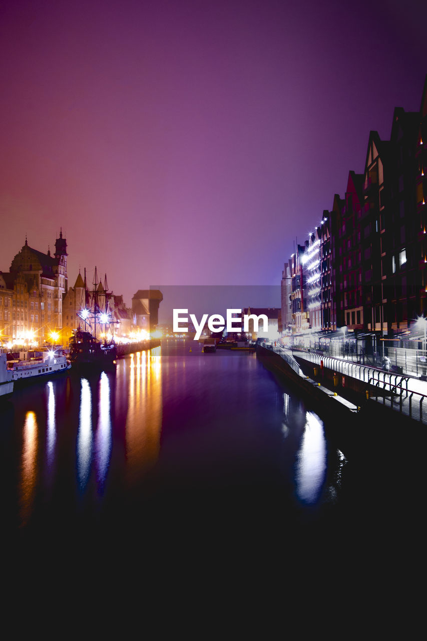 Illuminated buildings by river against clear sky at night