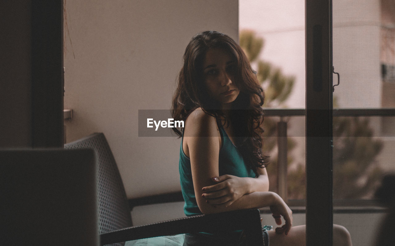 Portrait of beautiful sad woman sitting on armchair at home