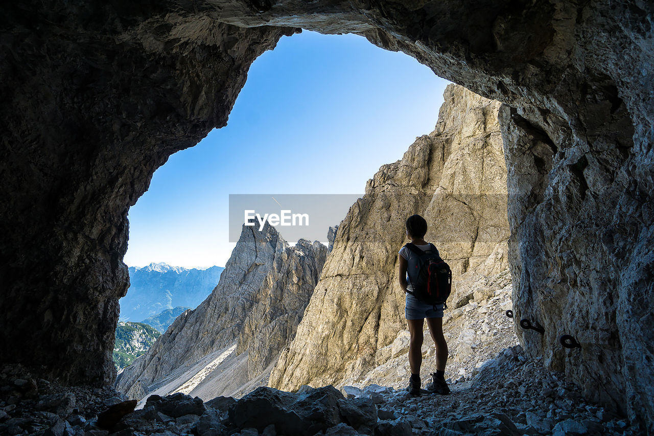 Rear view of woman with backpack standing in cave by mountains