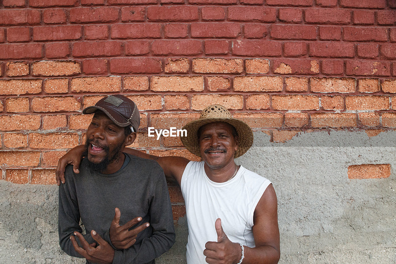 Portrait of man with friend standing against brick wall