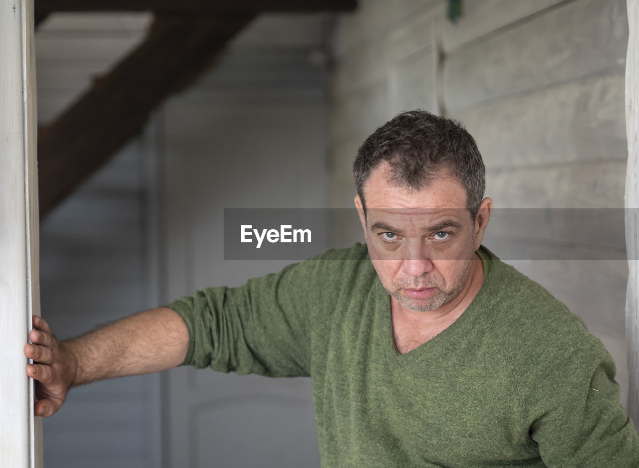 Portrait of serious mature man leaning on wall at home