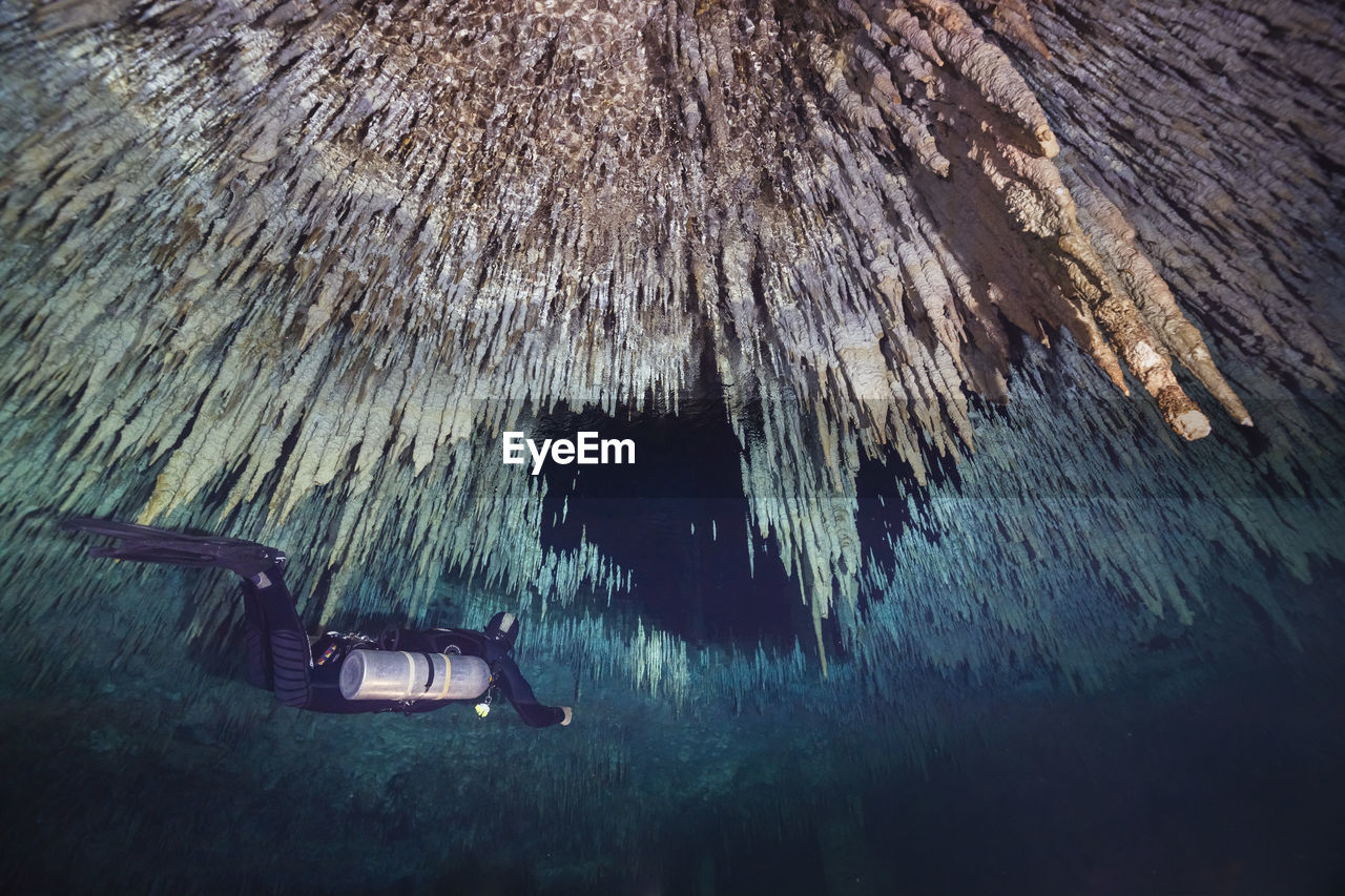 Low angle view of man scuba diving below stalactites in sea