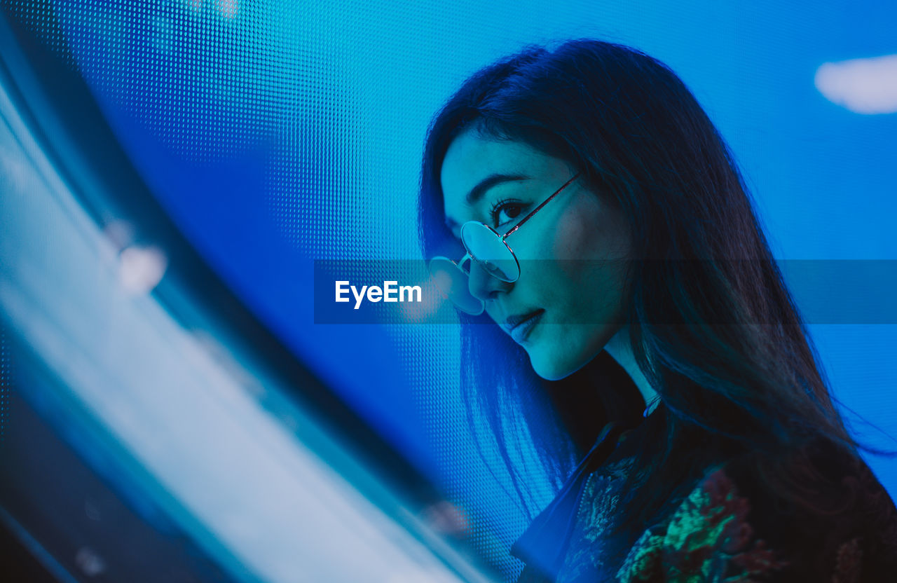 Close-up of young woman standing against illuminated city at night