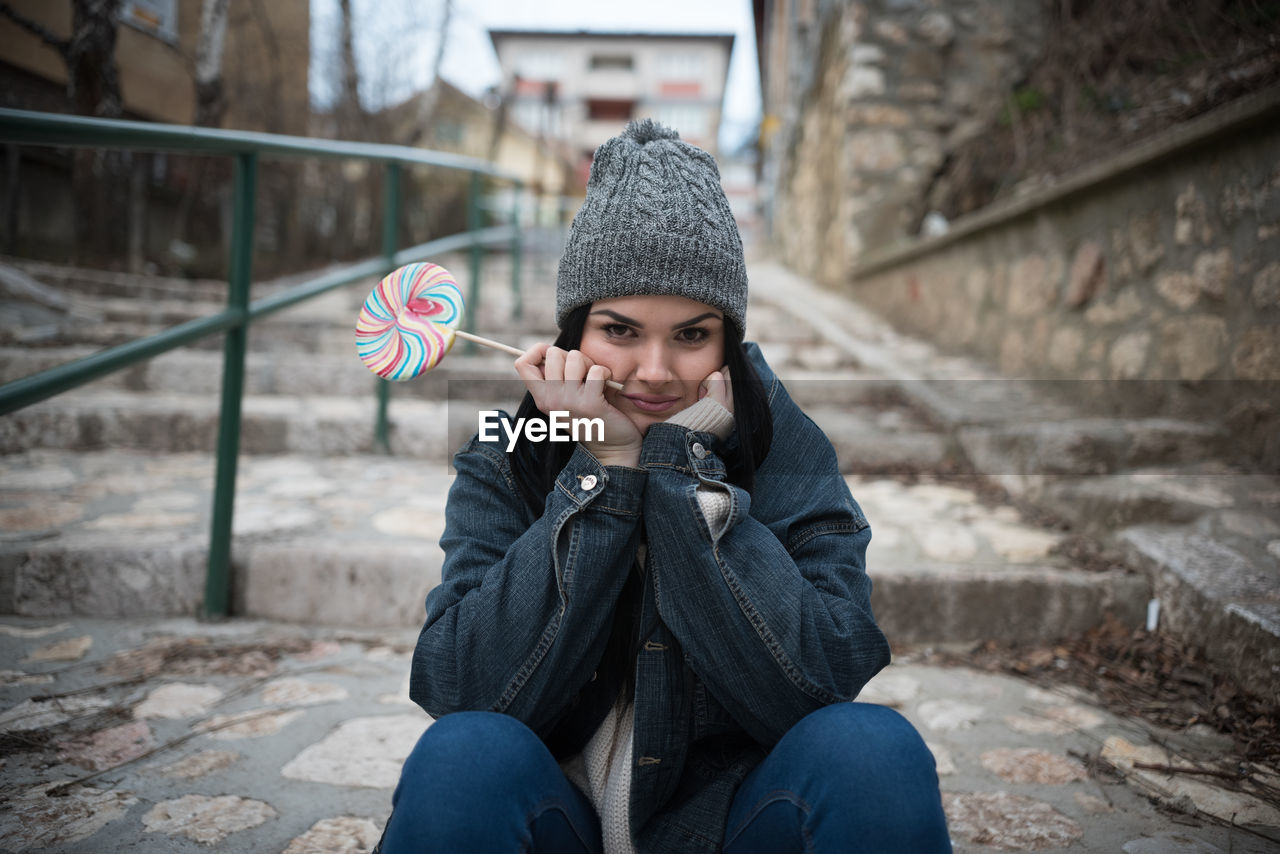 Portrait of young woman having lollipop while sitting on steps