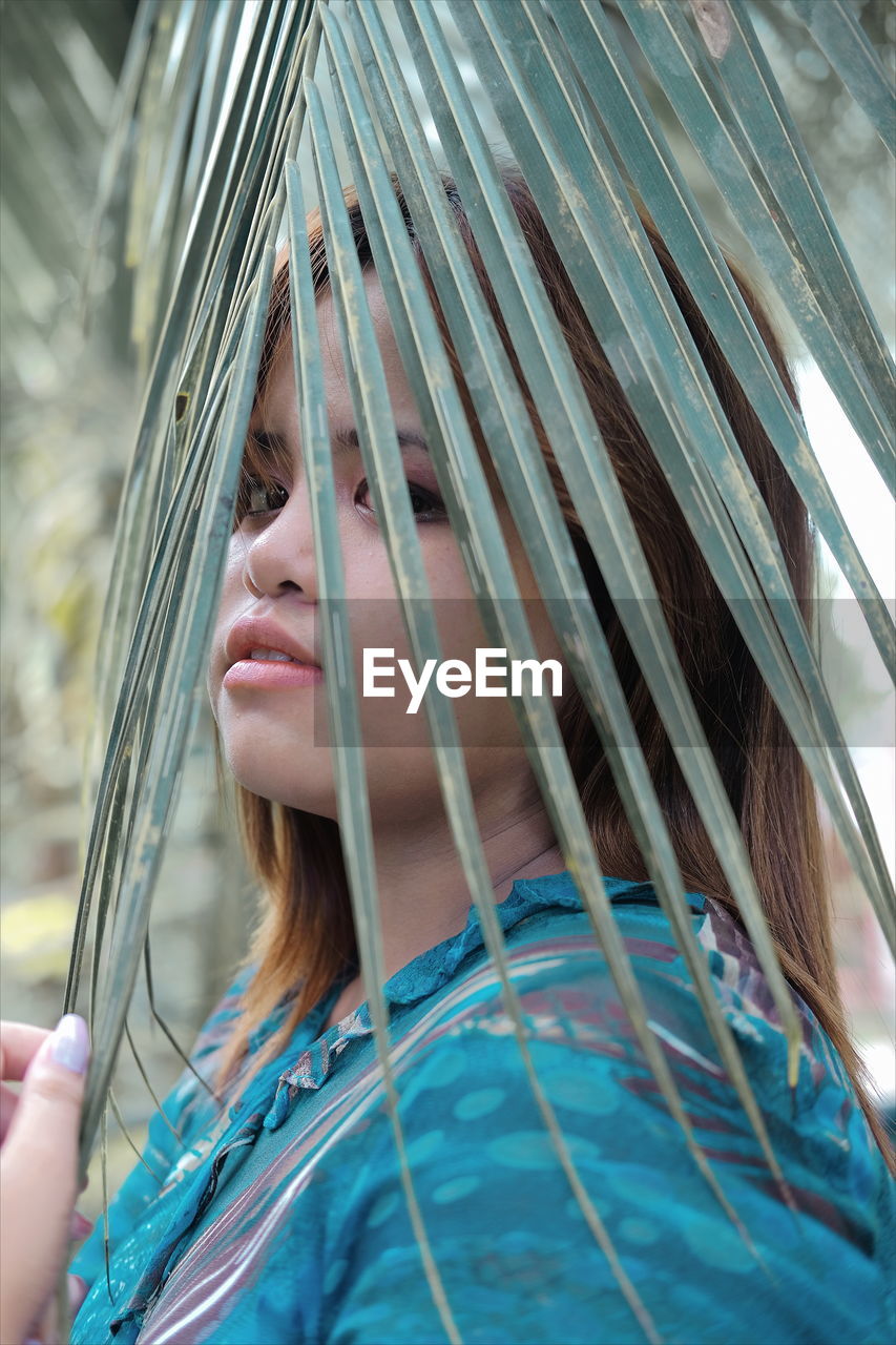 Close-up portrait of teenage girl looking through palm leaf