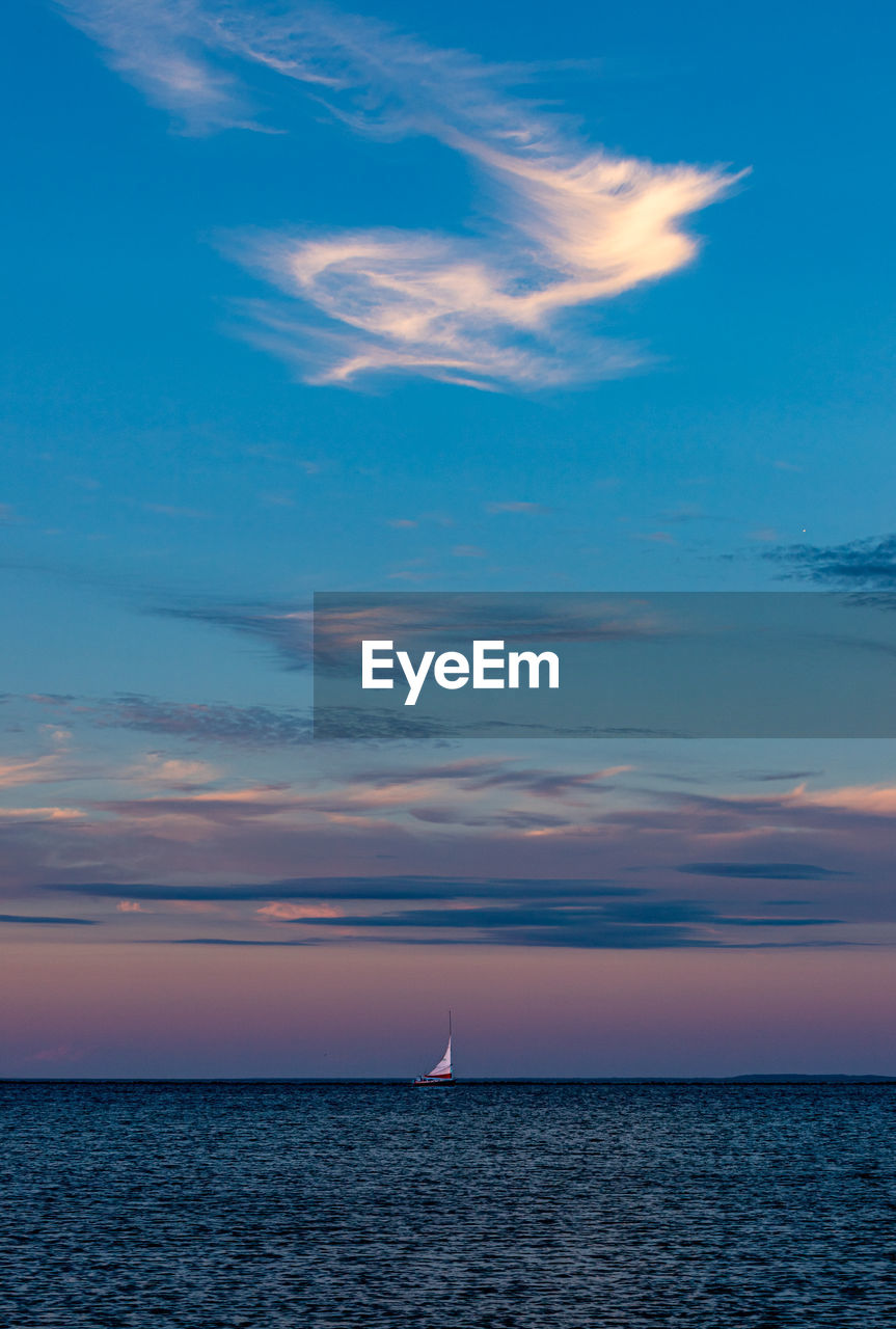 White sailboat isolated in ocean under beautiful sunset sky.