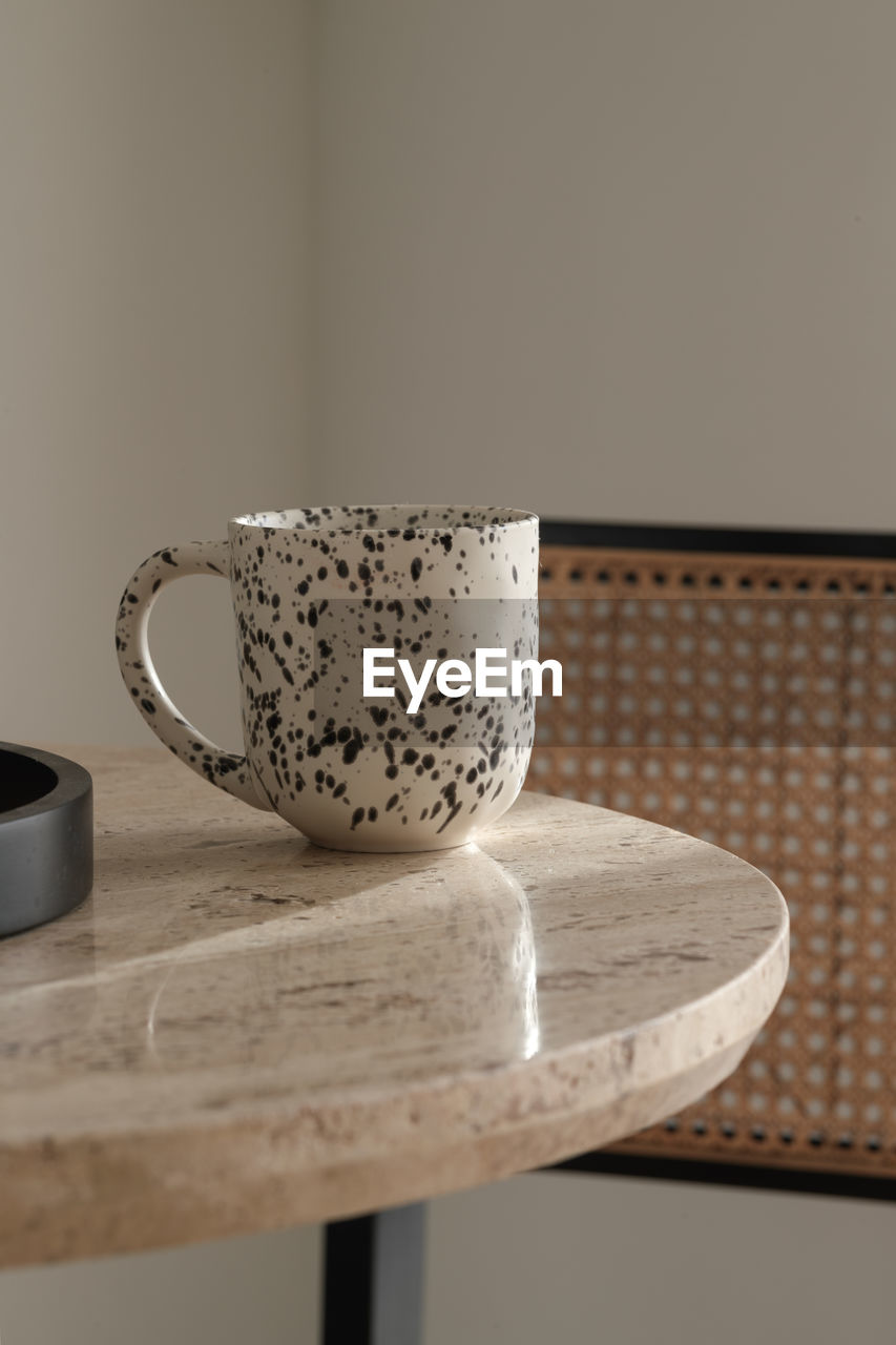 ceramic, indoors, cup, mug, table, no people, food and drink, still life, coffee cup, drink, tea cup, art, home interior, pattern, wood, close-up, crockery, refreshment, simplicity, porcelain, coffee, seat, tea, hot drink, domestic room, lighting, kitchen utensil, iron, furniture