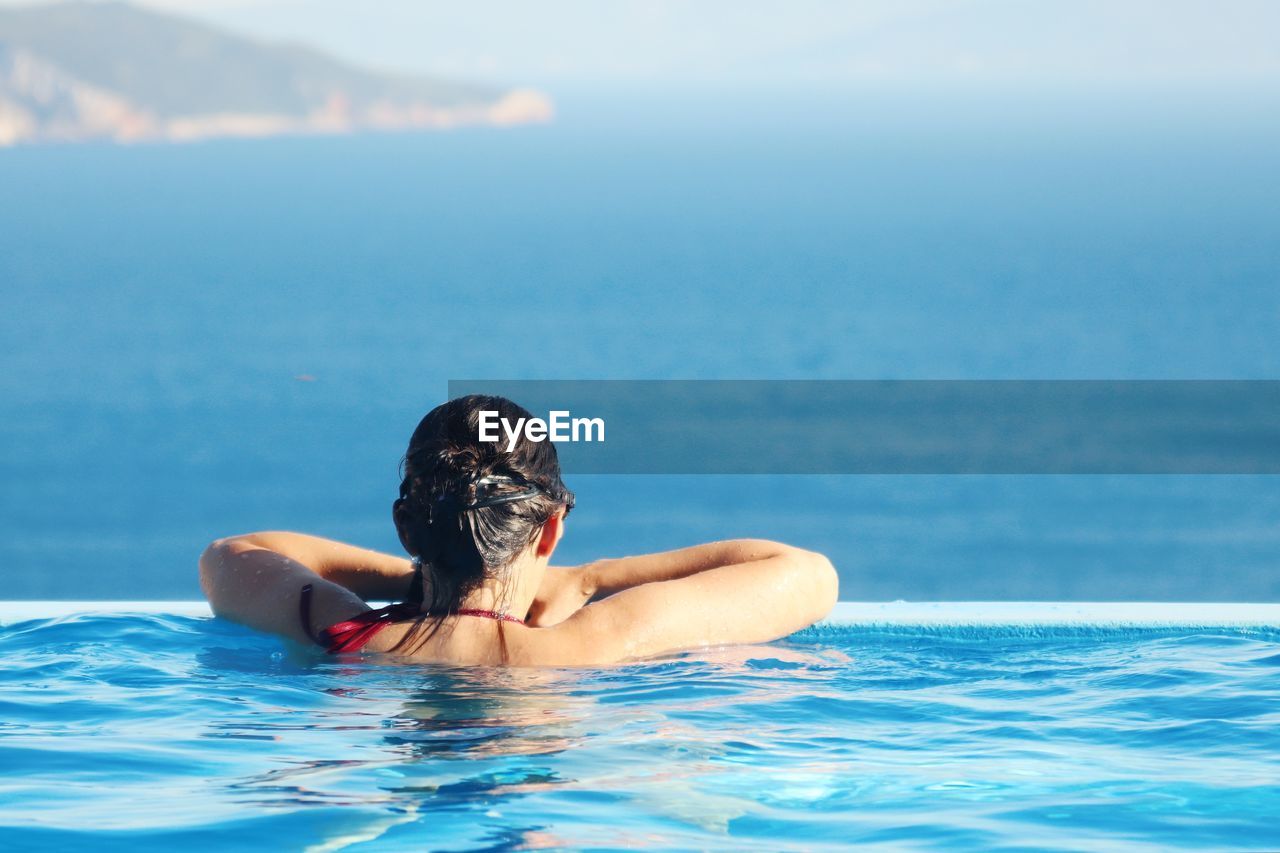 Rear view of woman in swimming pool looking at sea