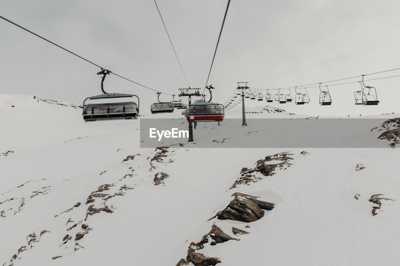 Ski lift over snow covered mountains against sky