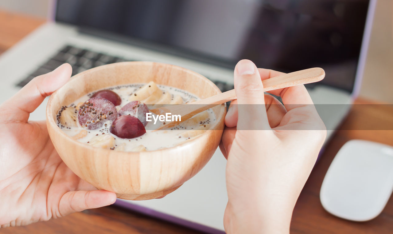 Close-up of hand holding bowl of milk and plum with chopped banana