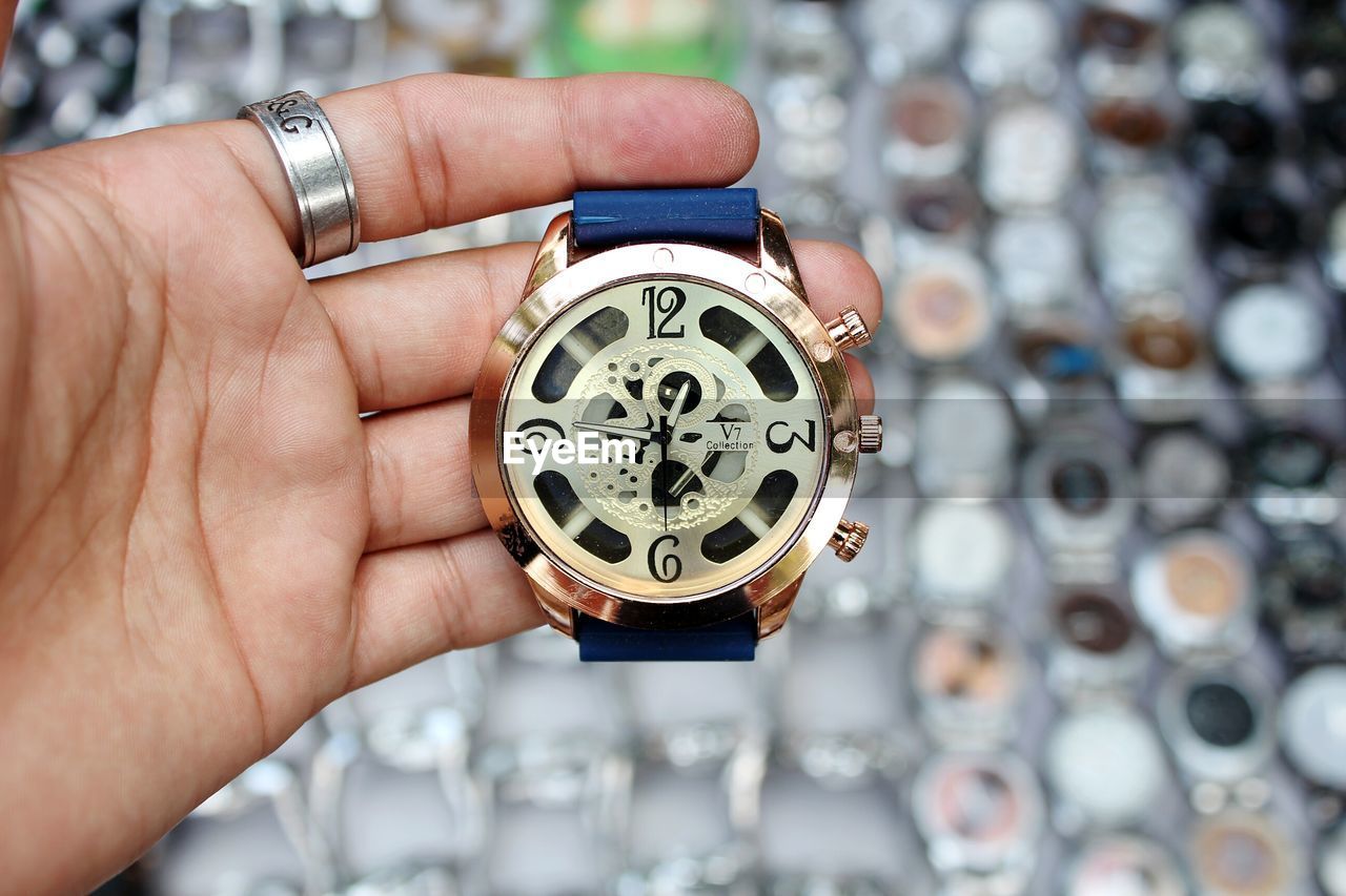 CLOSE-UP OF HUMAN HAND HOLDING CLOCK AGAINST BLURRED BACKGROUND