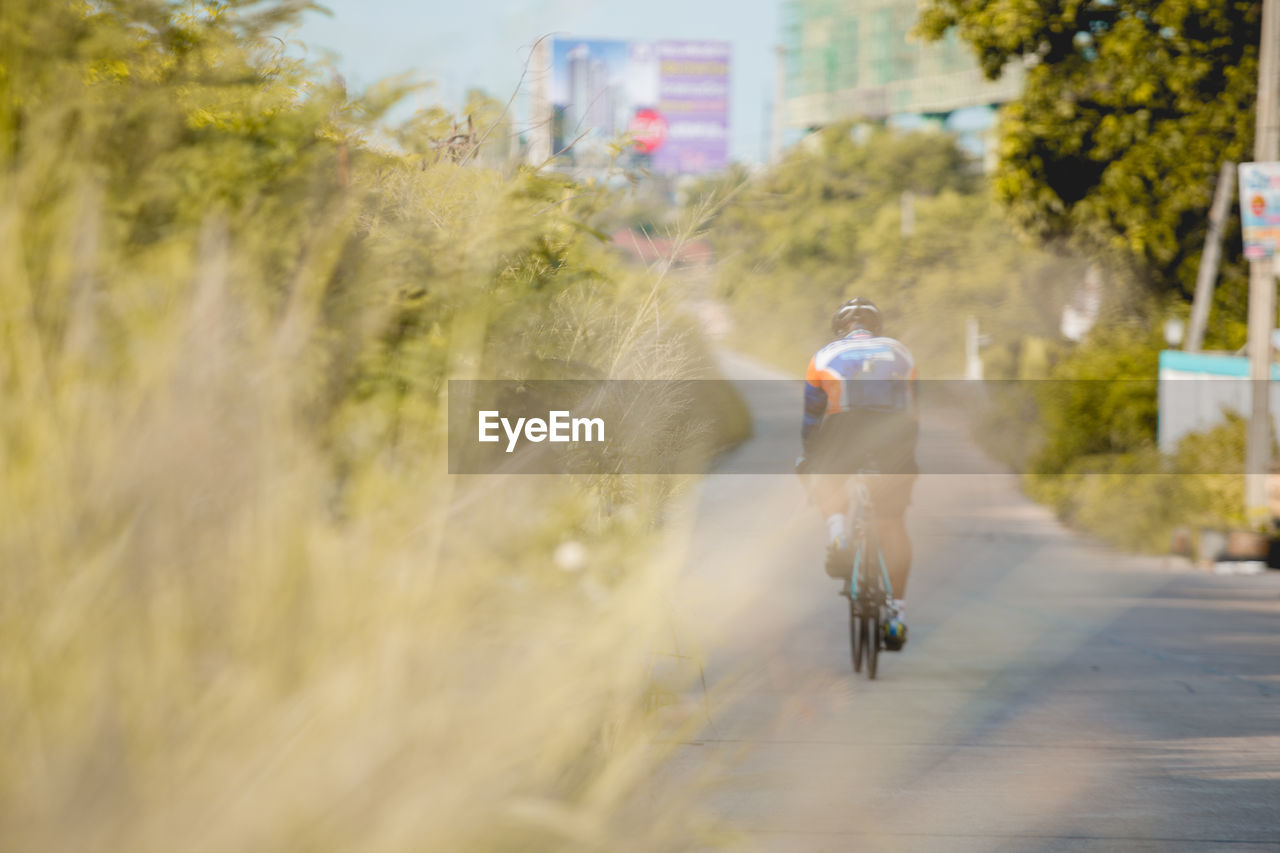 FULL LENGTH REAR VIEW OF MAN RIDING BICYCLE ON ROAD