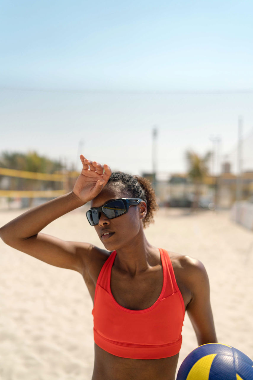 sports, adult, one person, women, clothing, lifestyles, exercising, beach, volleyball, beach volleyball, land, sports clothing, young adult, nature, leisure activity, day, glasses, athlete, sunlight, net sports, sand, summer, sunglasses, sky, outdoors, focus on foreground, copy space, water, waist up, arm, vitality, front view, relaxation, standing, ball, limb, fashion, sports equipment, sea, swimwear, activity, female, sports training, strength, human limb, vacation, trip, looking, muscular build, motion, portrait