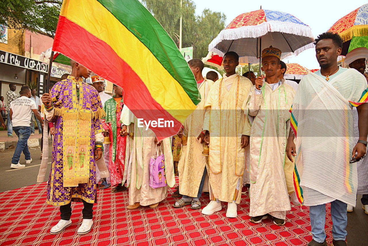 group of people, adult, umbrella, men, women, multi colored, day, clothing, crowd, large group of people, tradition, traditional clothing, city, celebration, outdoors, street, architecture, person, lifestyles, parasol, event, protection, togetherness, standing, walking, nature