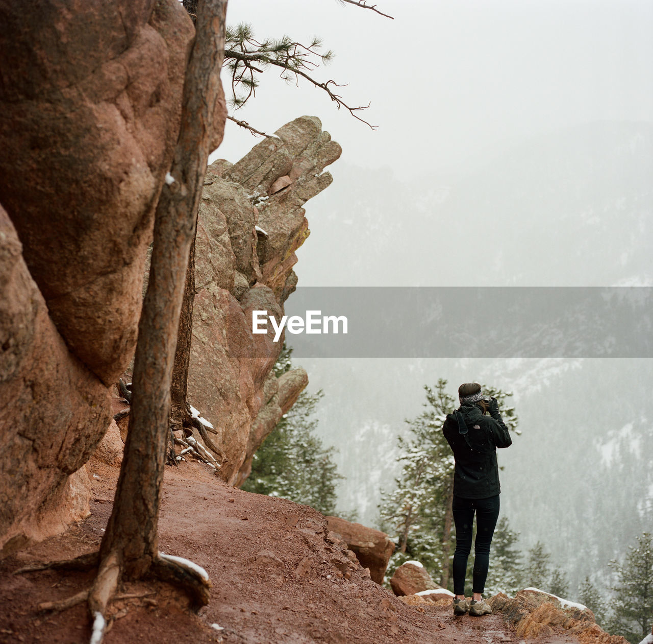 REAR VIEW OF MAN STANDING ON ROCK LOOKING AT VIEW