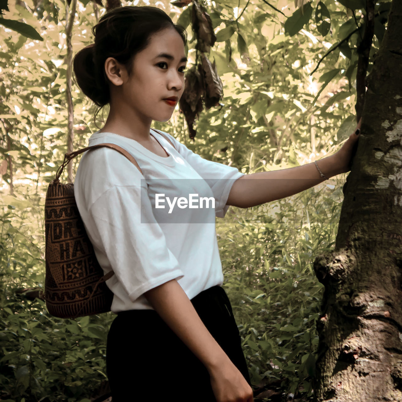 Teenage girl looking away while standing against tree trunk