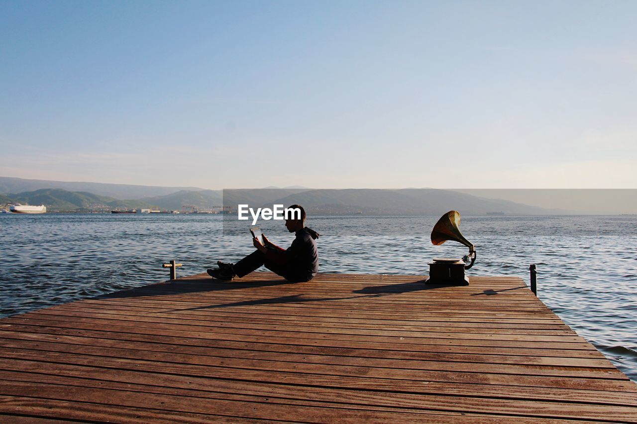 REAR VIEW OF MAN SITTING ON PIER