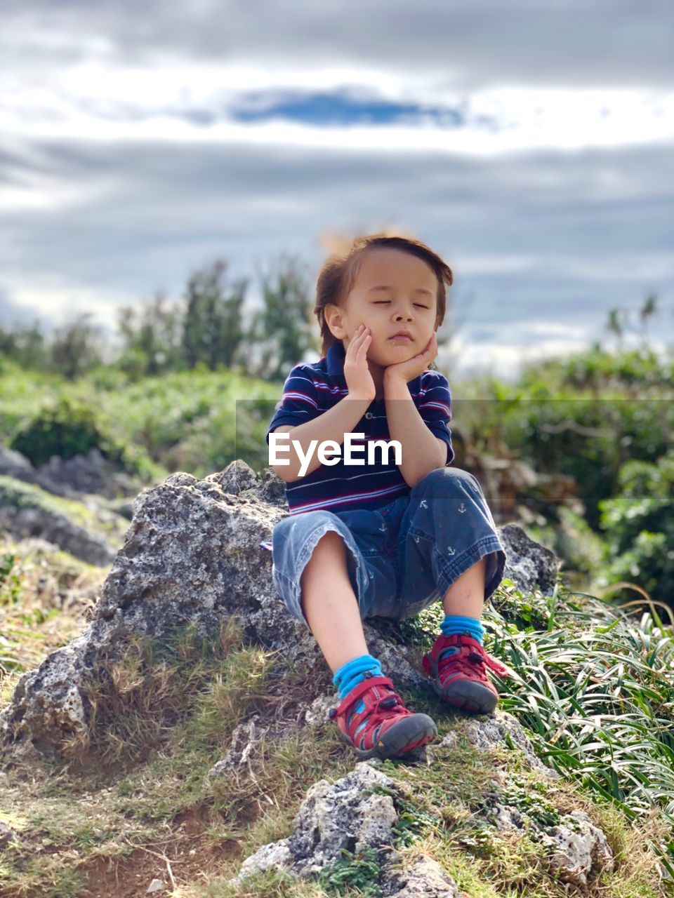 Thoughtful boy with eyes closed sitting on rock