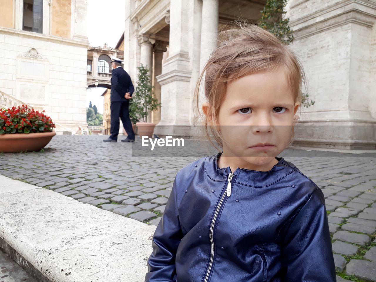 Portrait of girl sulking sitting against built structure in city