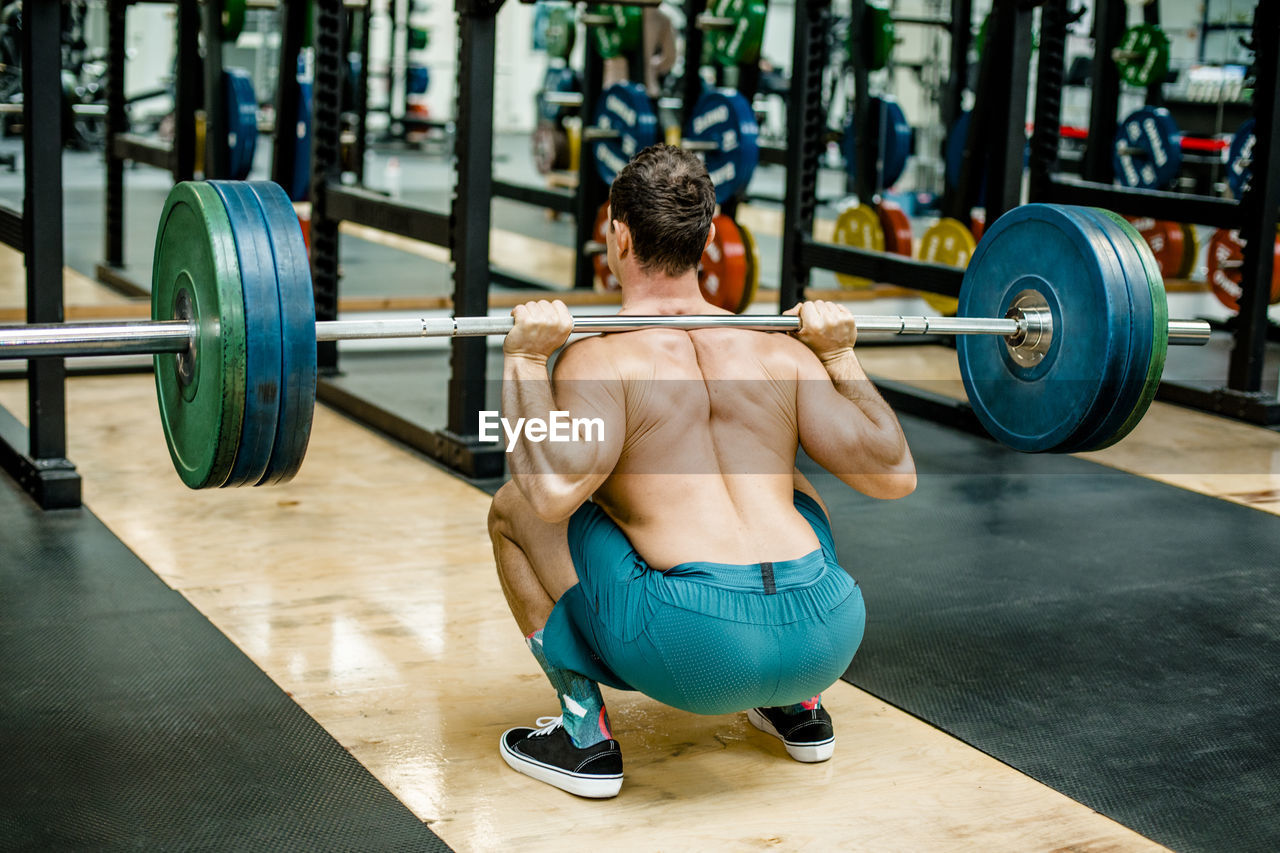 Man in squatting position weightlifting at gym