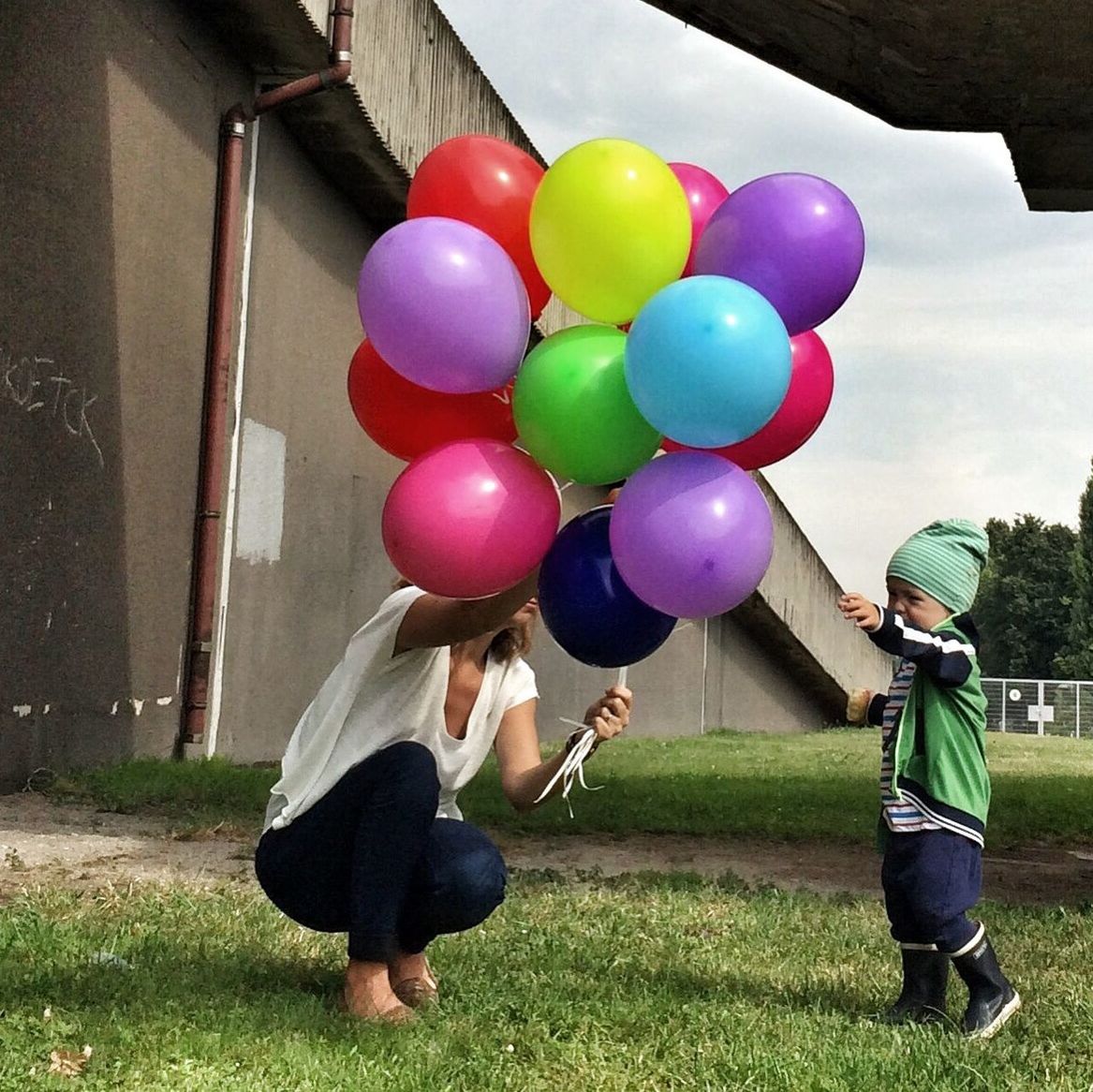 Mother and son with multi colored balloons at grassy field against sky