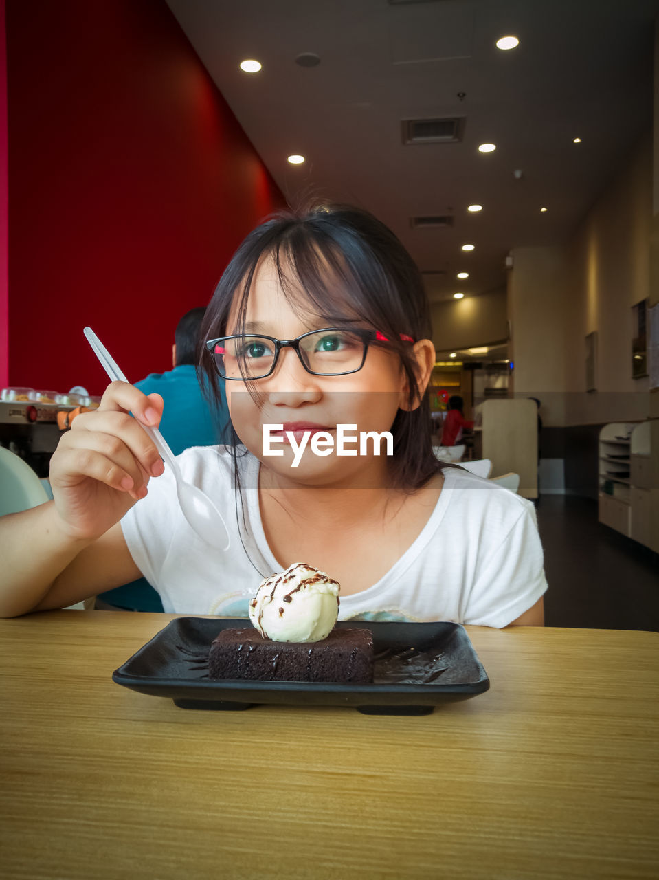 PORTRAIT OF YOUNG WOMAN HOLDING EYEGLASSES ON TABLE AT ILLUMINATED RESTAURANT