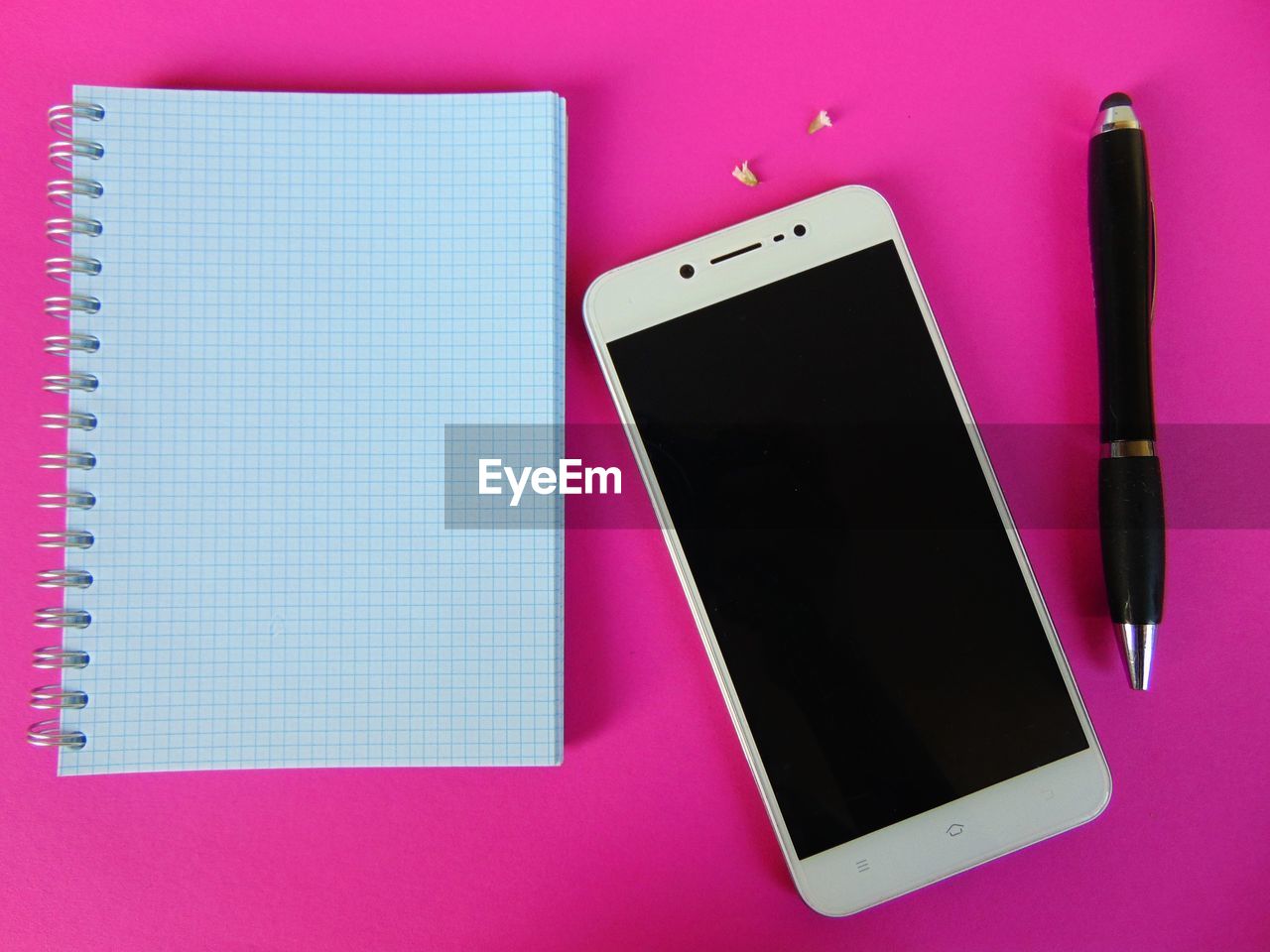 Directly above view of pen and blank diary with mobile phone on pink background