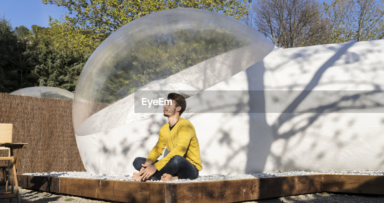 Young man enjoying sunlight in front of transparent dome hotel