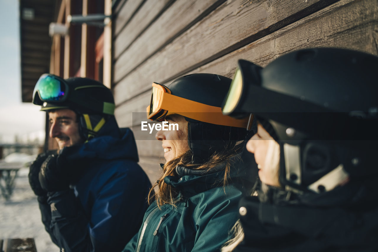 Smiling friends wearing sports helmets at ski resort during sunset