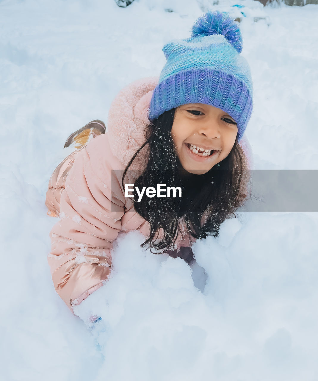 Diverse mixed race pre school toddler girl outdoors in winter playing with snow 