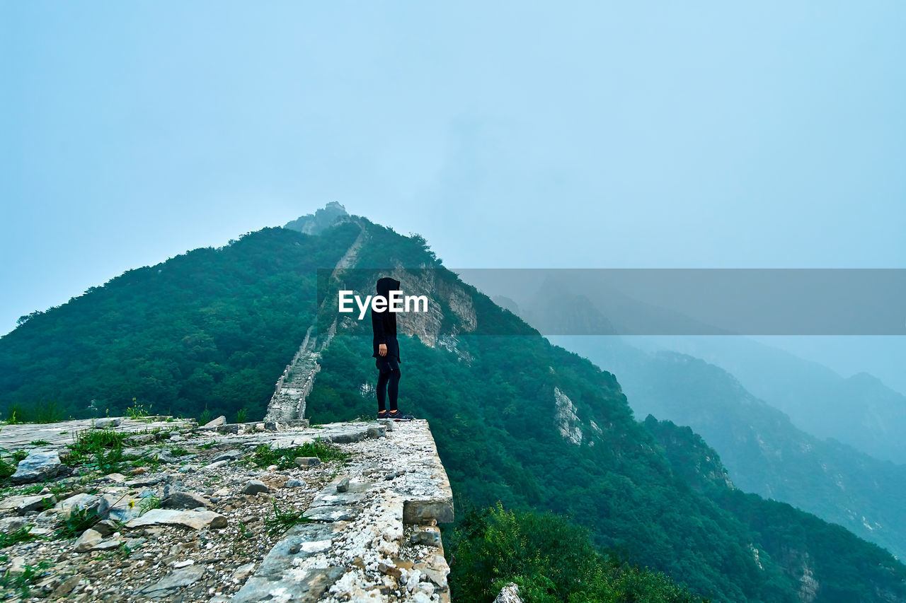 Side view of man standing on mountain against sky