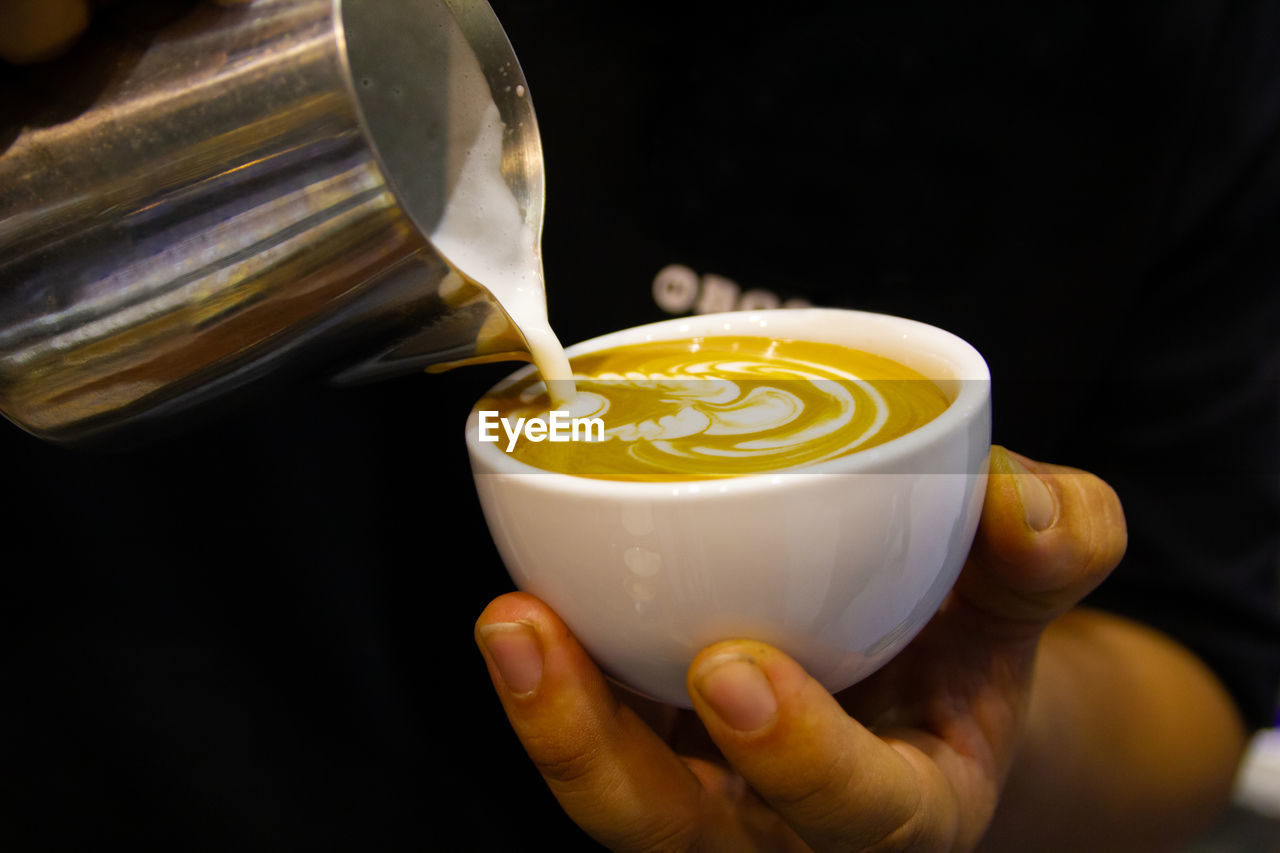 Barista making cappuccino in his coffee shop or cafe, barista pouring latte froth to make a coffee.