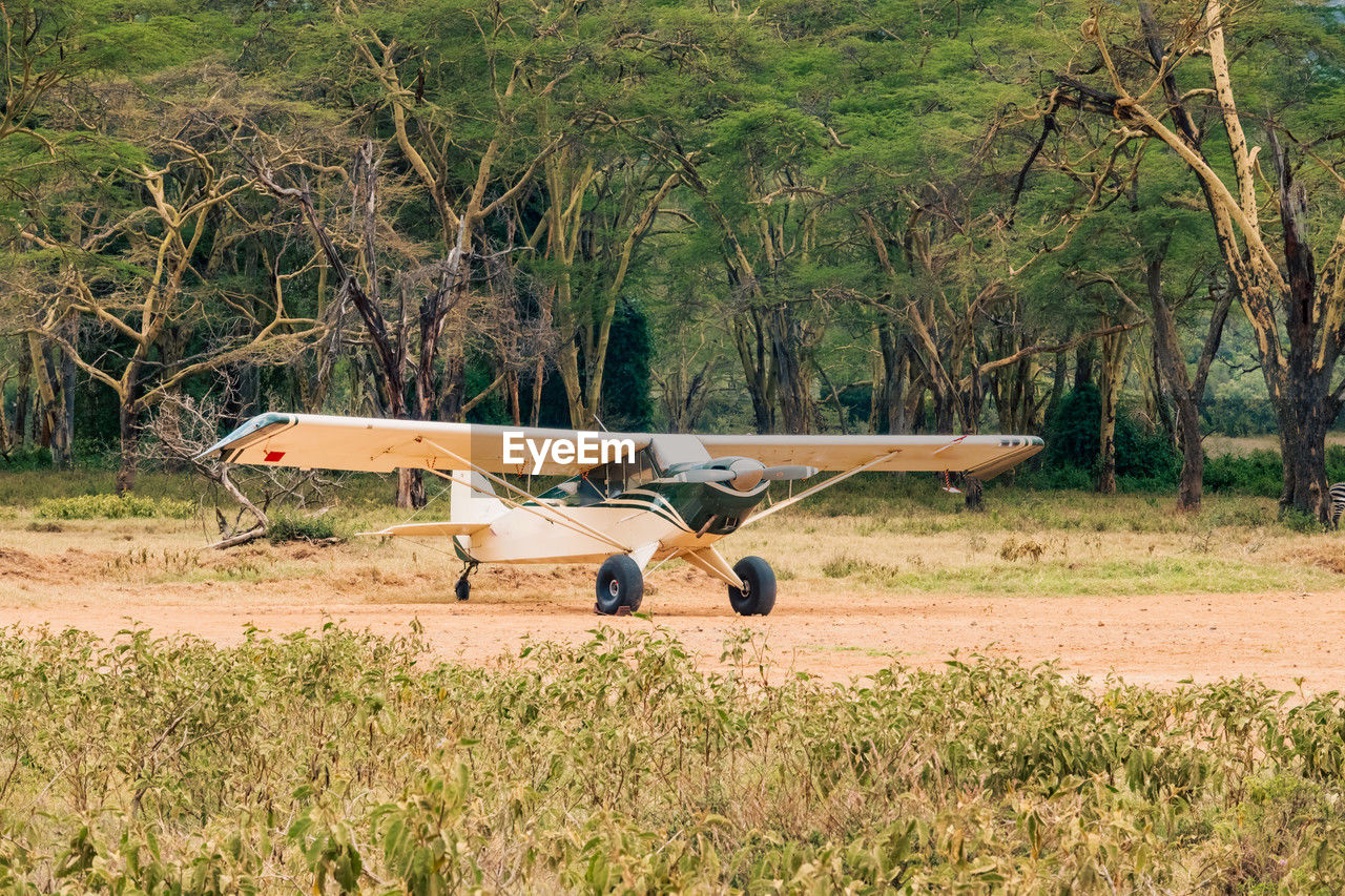 A light aircraft on a dirt airstrip amidst acacia trees at lake nakuru national park in kenya
