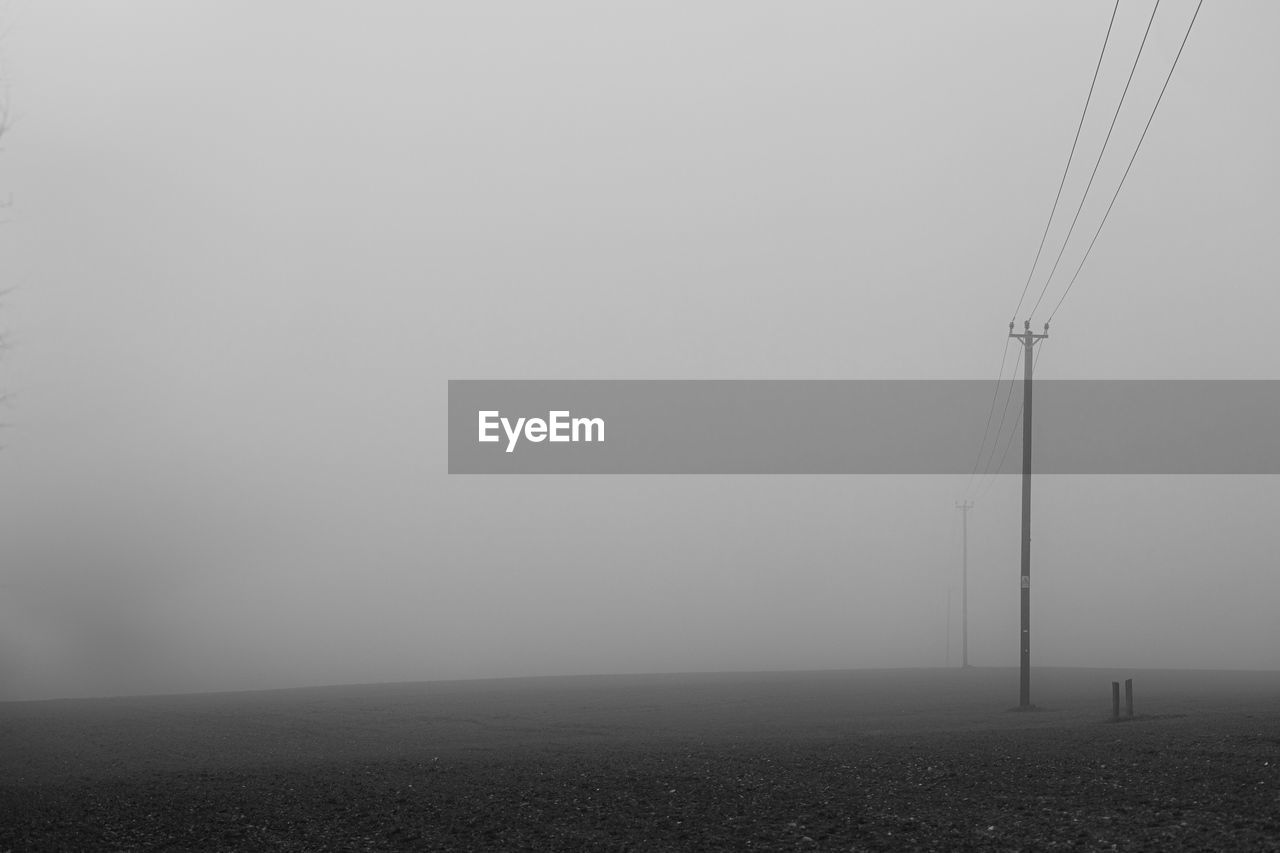 ELECTRICITY PYLON ON FIELD AGAINST SKY