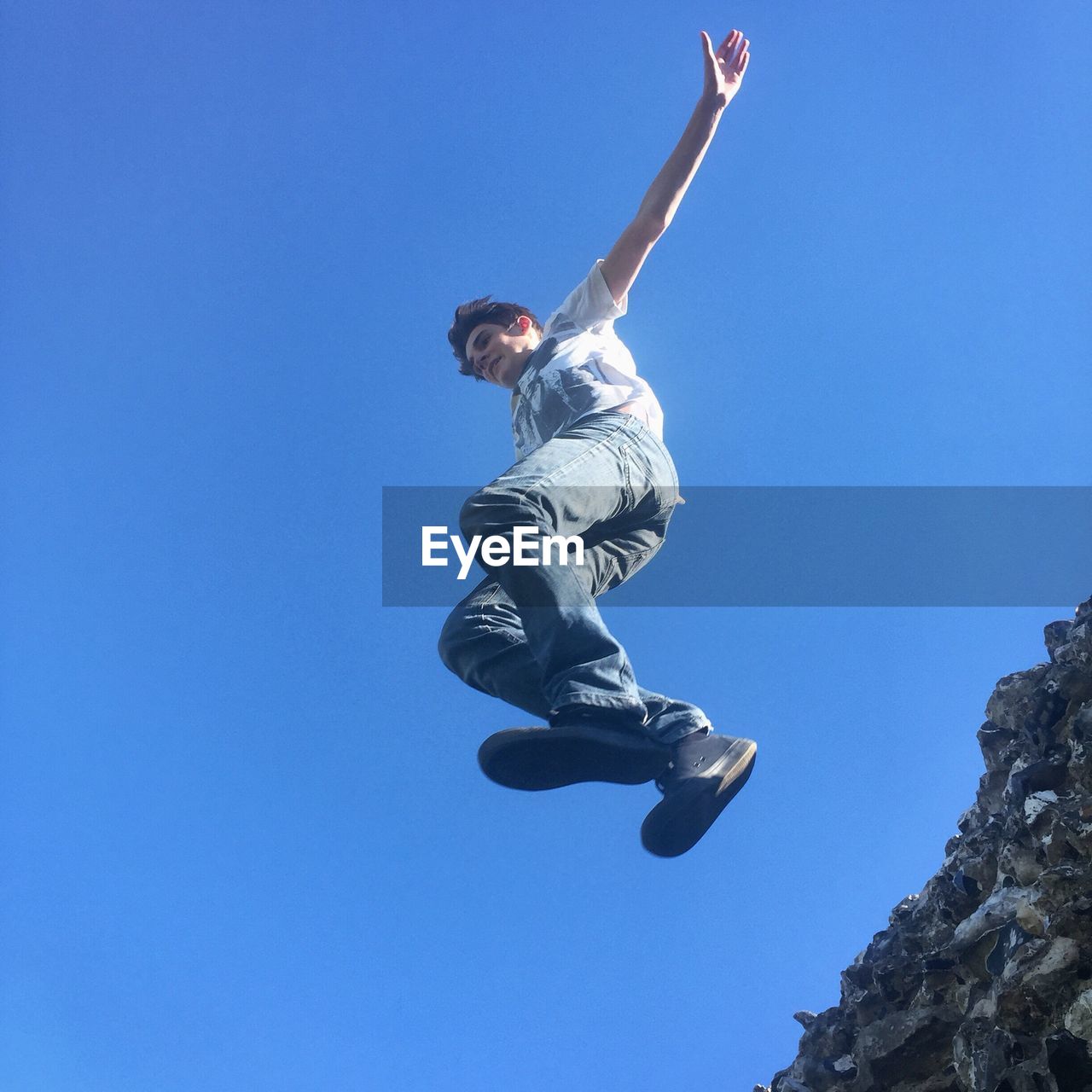 Low angle view of boy jumping from retaining wall against clear blue sky