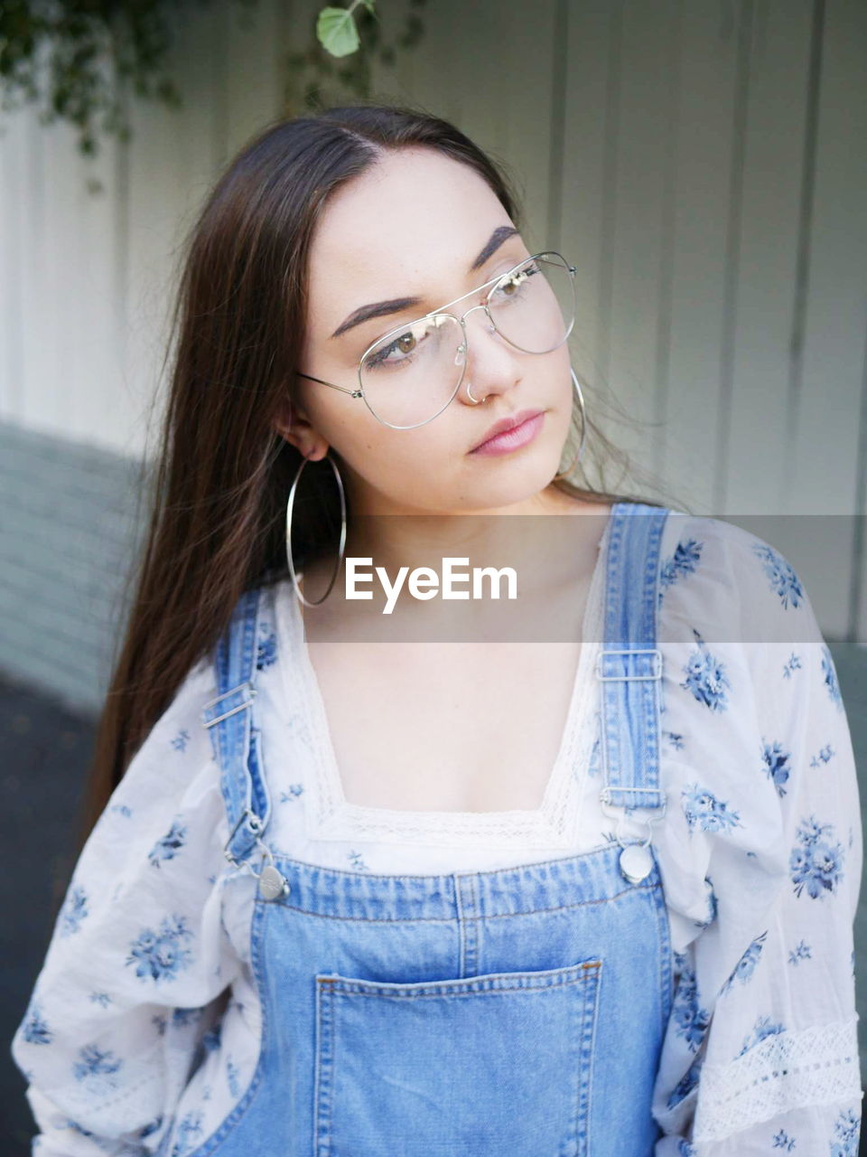 Thoughtful beautiful woman wearing eyeglasses while standing against wall