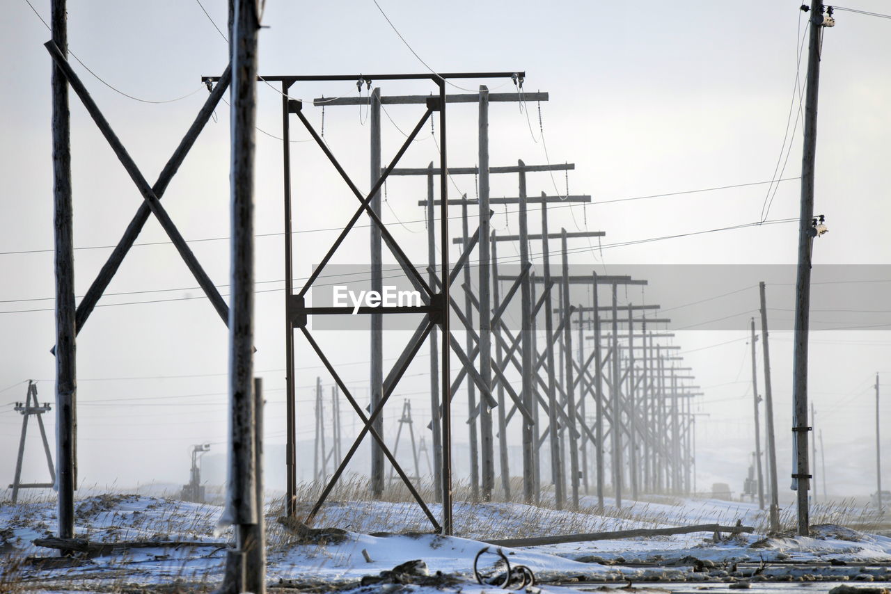 Electricity pylons on snow covered field against clear sky during winter