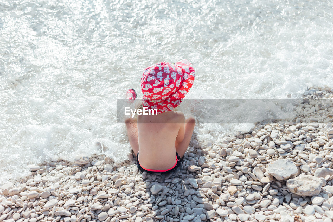 High angle view of shirtless girl sitting on shore at beach