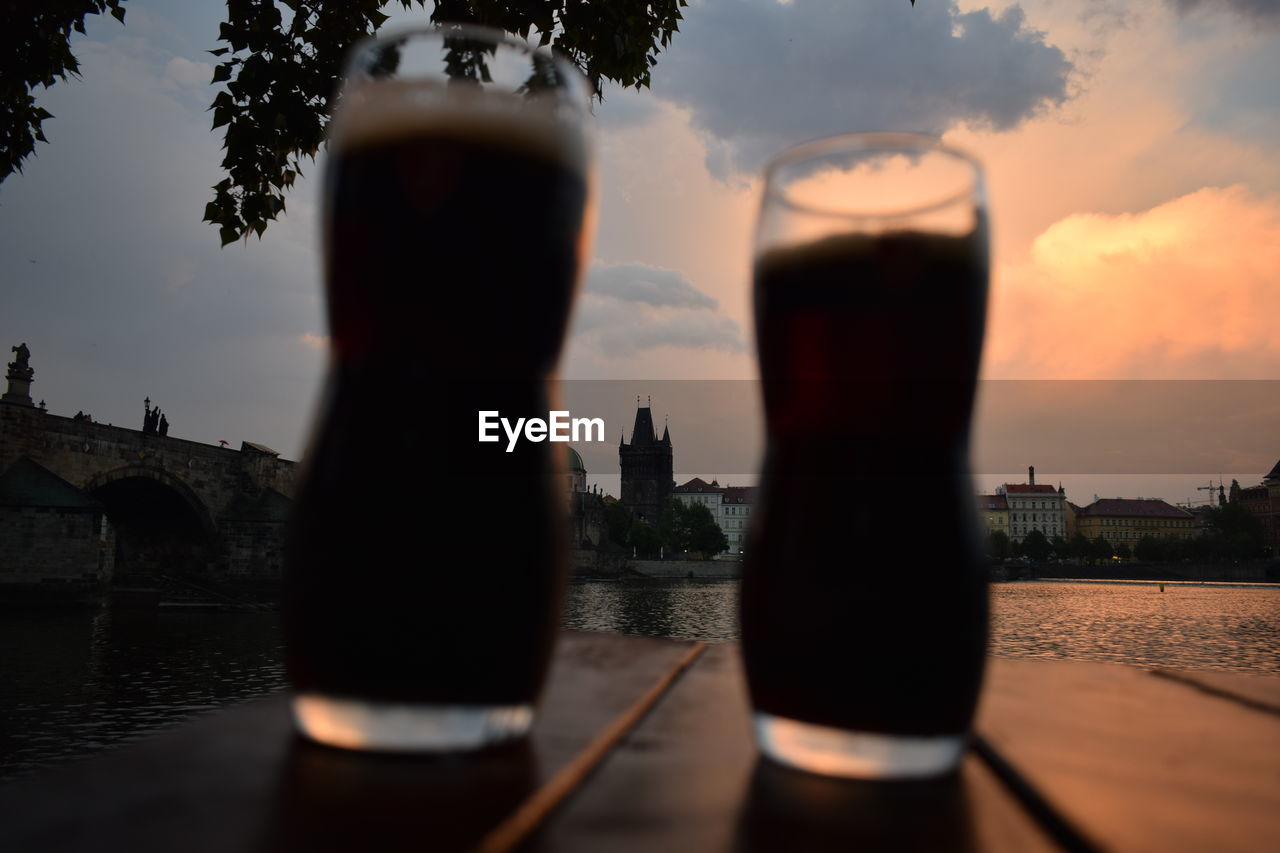 Close-up of beer glasses against river at sunset