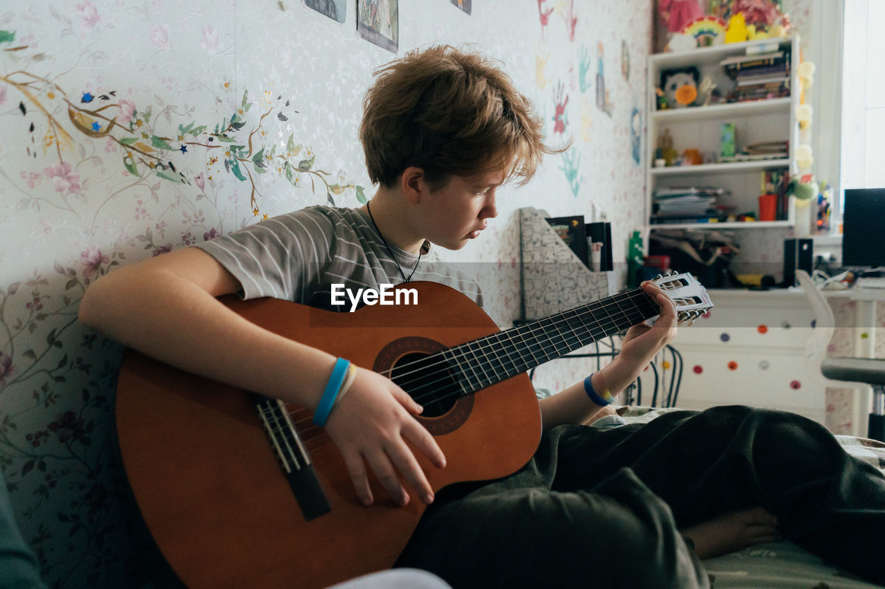 Teenage girl sitting on the bed learning to play the guitar.