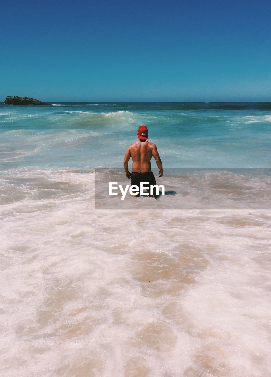 Rear view of shirtless man standing in sea against clear sky