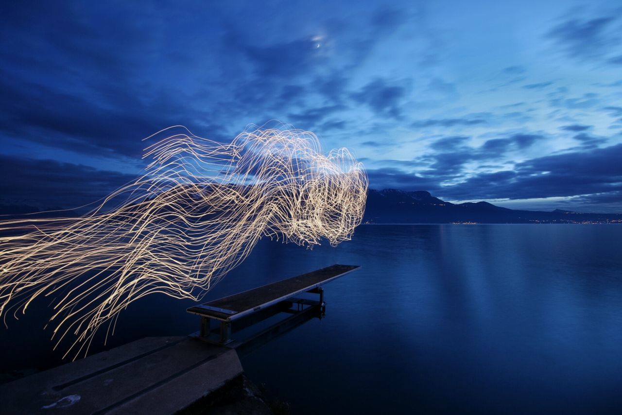 Light trails on jetty in sea against sky