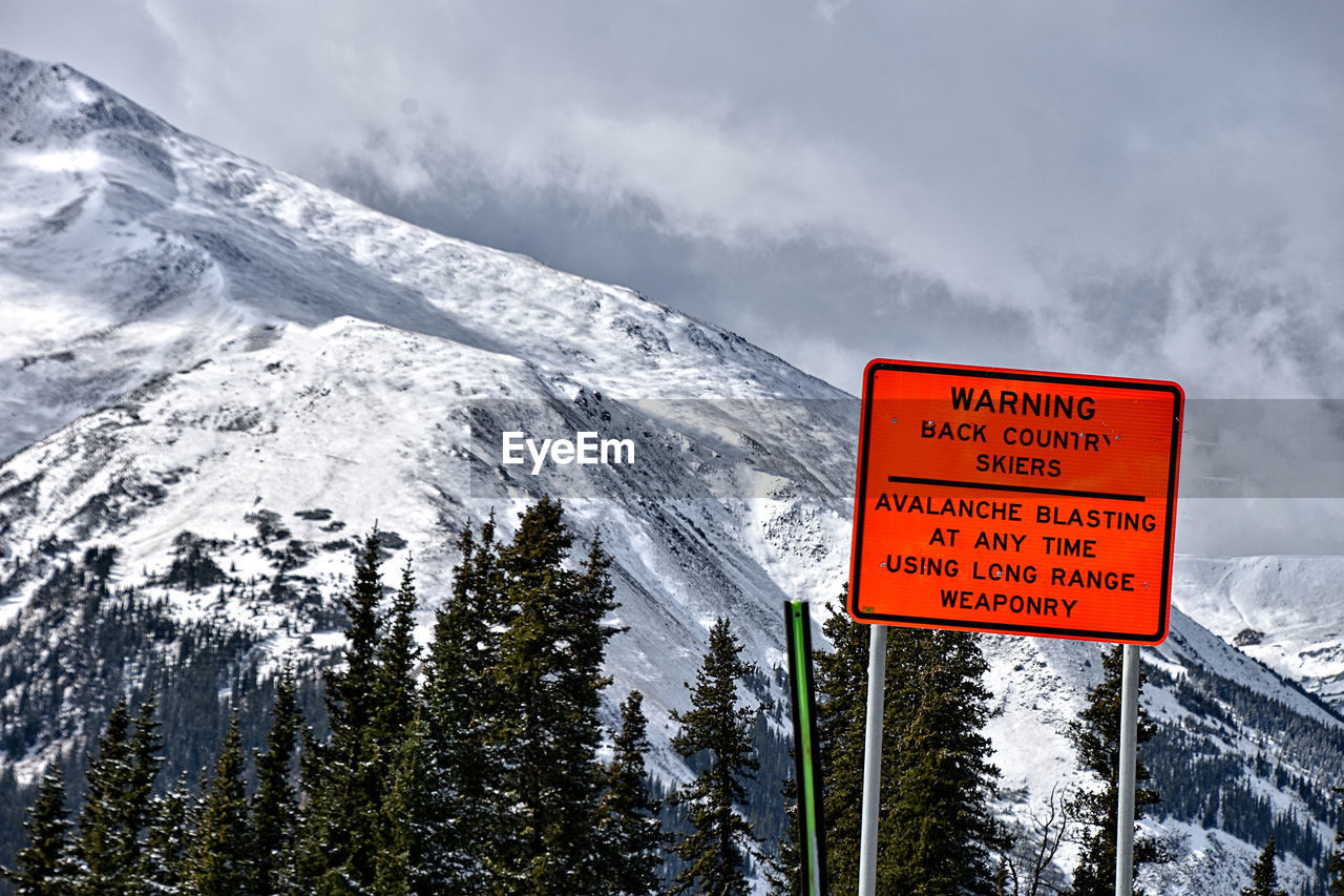 INFORMATION SIGN BY SNOWCAPPED MOUNTAIN AGAINST SKY