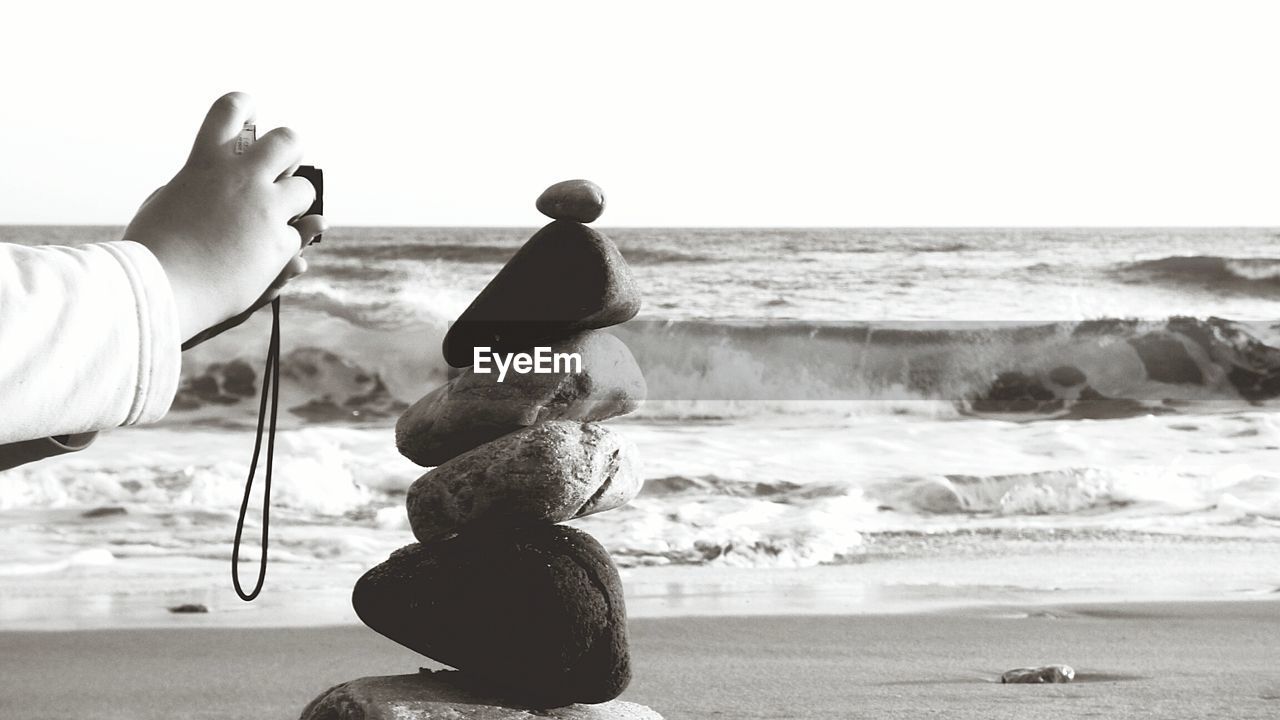 Cropped hands photographing stack of stones at beach