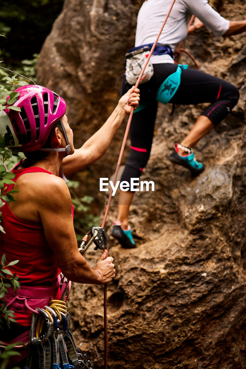 Low angle view of active senior male and female climbers climbing on rocky cliff