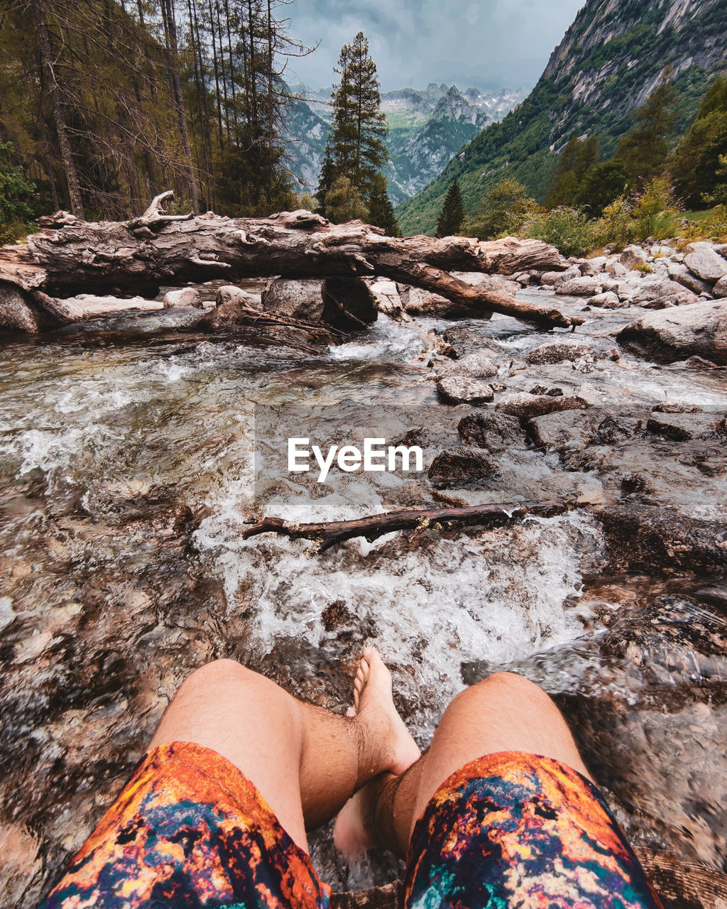 Low section of man sitting on rock in stream against mountain